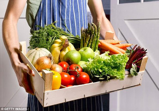 Man carrying a crate of vegetables and fruits.